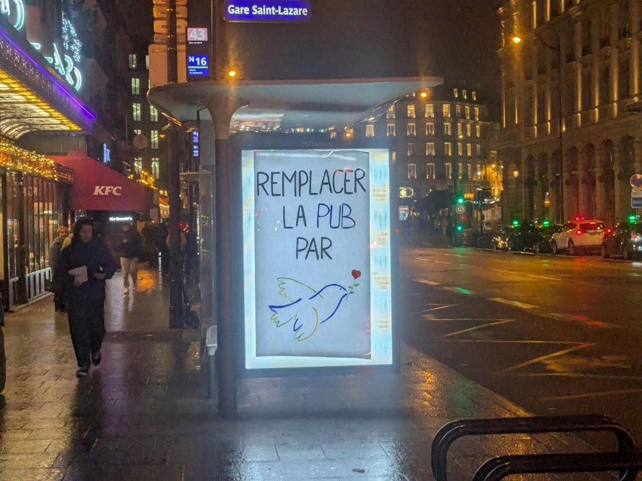 Une pub sur un arrêt de bus, remplacée par une affiche faite à la main, marquée "remplacer la pub par" et un dessin de colombe de la paix
