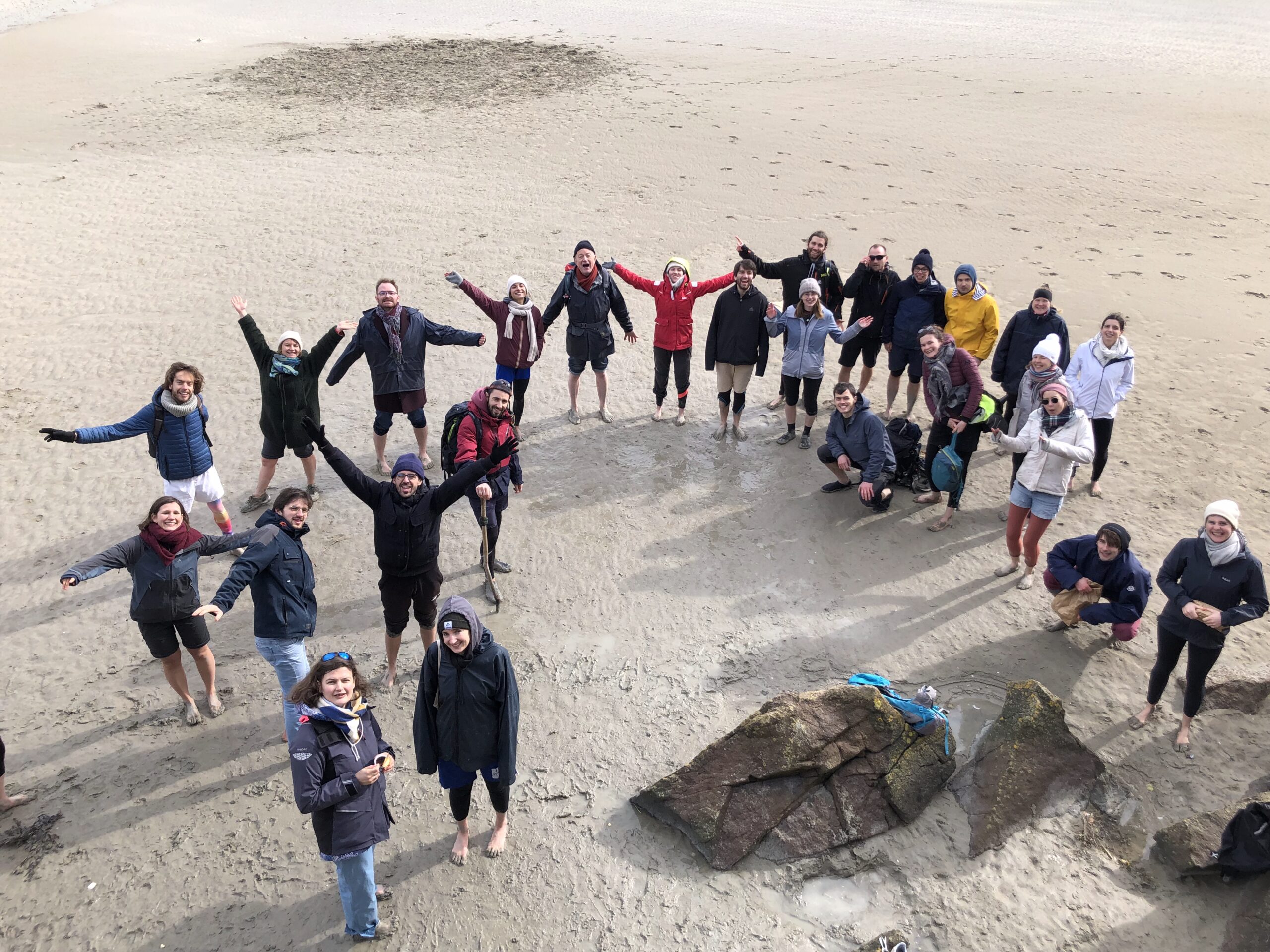 un groupe de membres de Lutte et Contemplation lèvent les bras sur la plage, en contre plongée