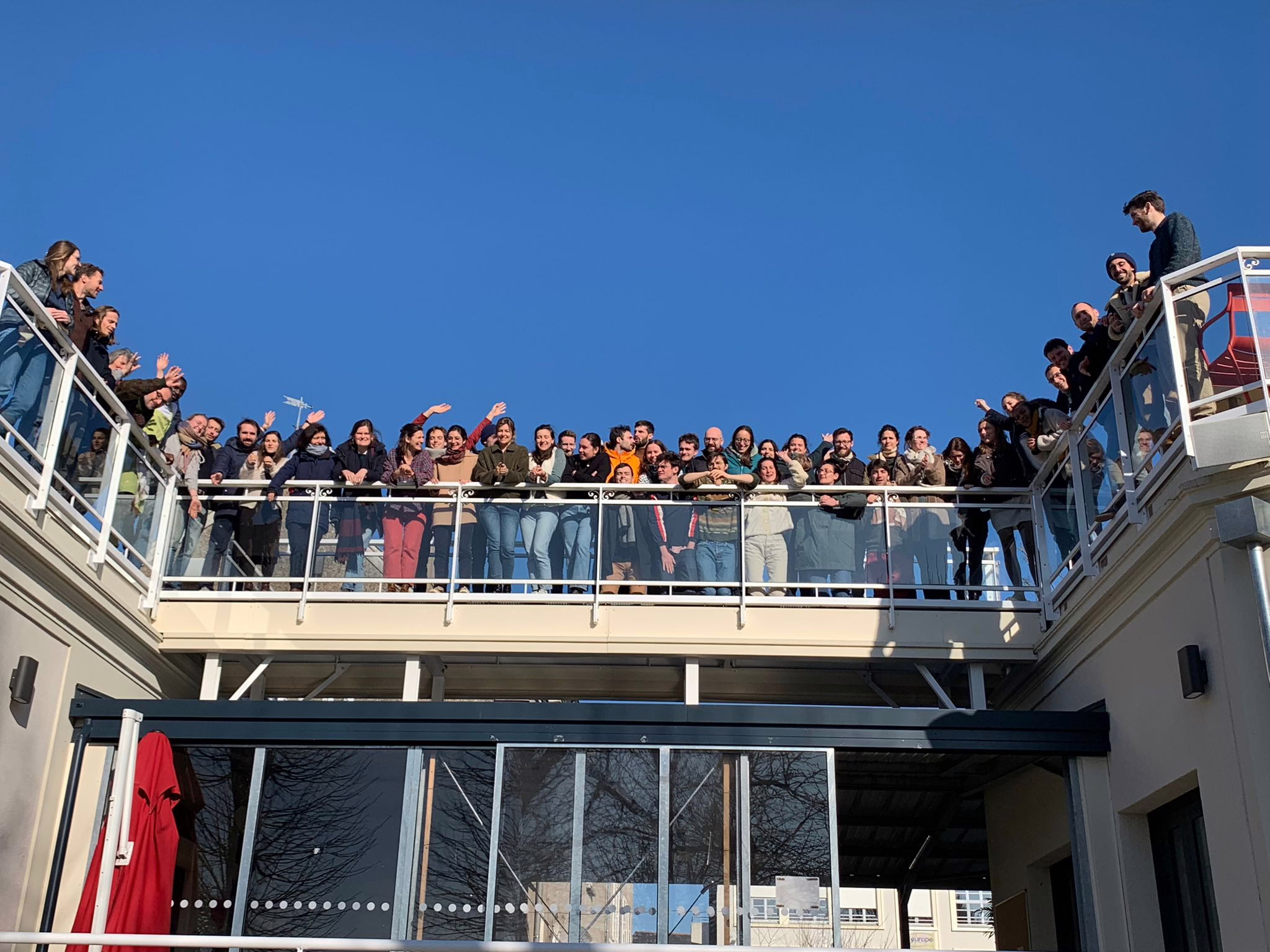 une soixantaine de membres de Lutte et Contemplation debout contre la rambarde d'une terrasse, sourient au photographe dans la lumière rasante d'hiver, sur un fond de ciel bleu sans nuage